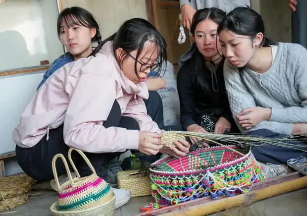 Students learning to weave a grass basket alongside village makers