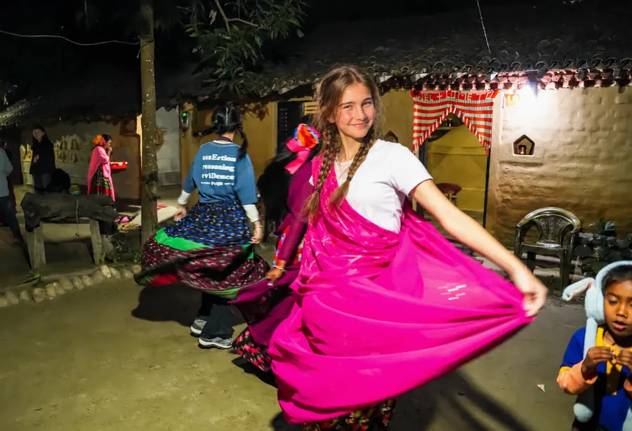 A student dancing in a borrowed Tharu skirt in a village courtyard at night