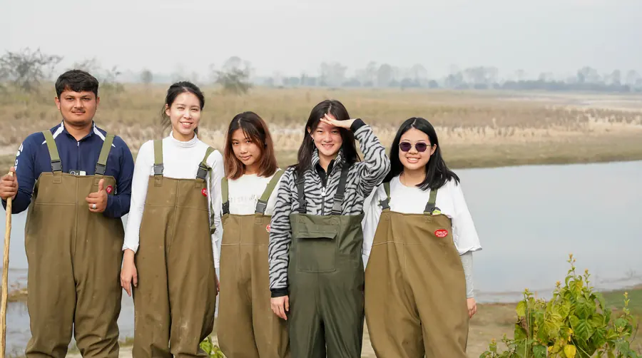 Five students in chest waders beside the river at Bardiya with a Nepali field guide