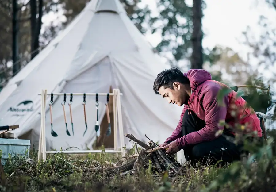 A guide laying a fire beside a bell tent pitched in pine forest
