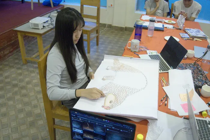 A student drawing a pangolin beside a laptop of camera-trap images at the CCCT