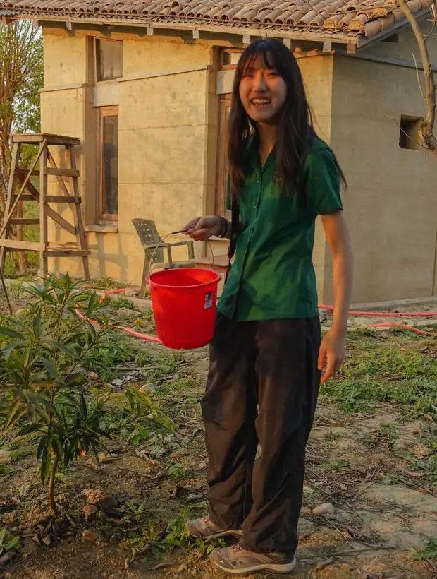 A student carrying a bucket outside a mud-walled building in Bardiya