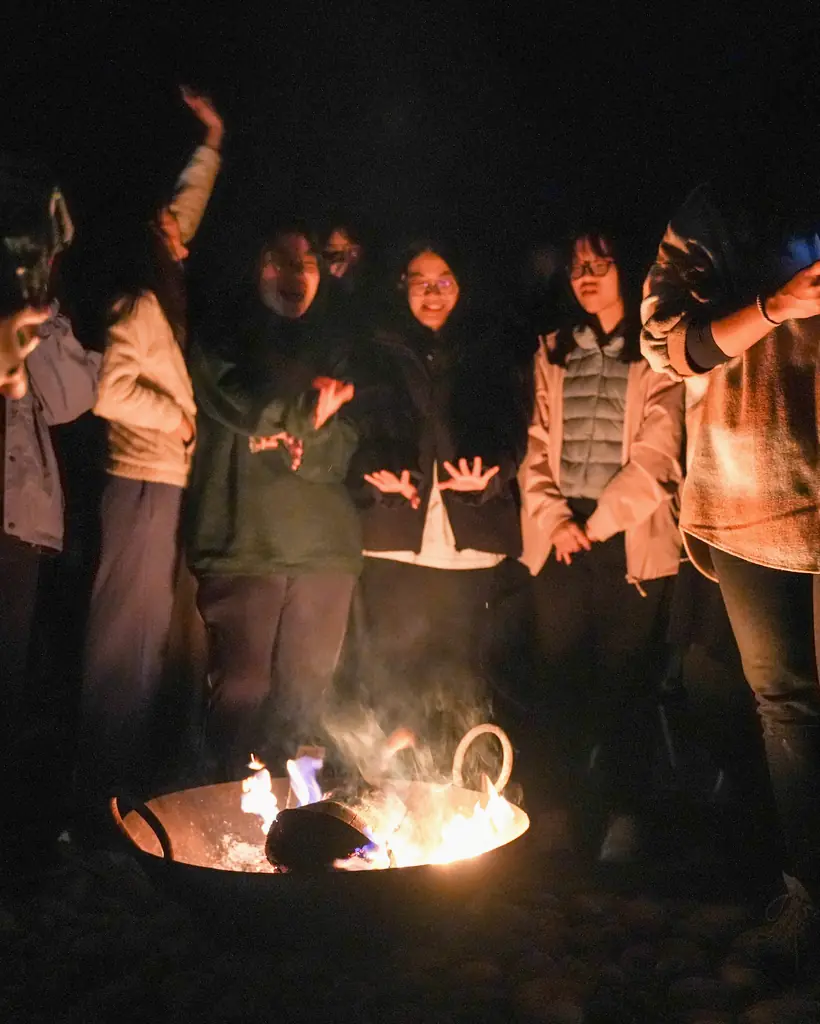 Students warming their hands around a fire bowl at night in Bardiya